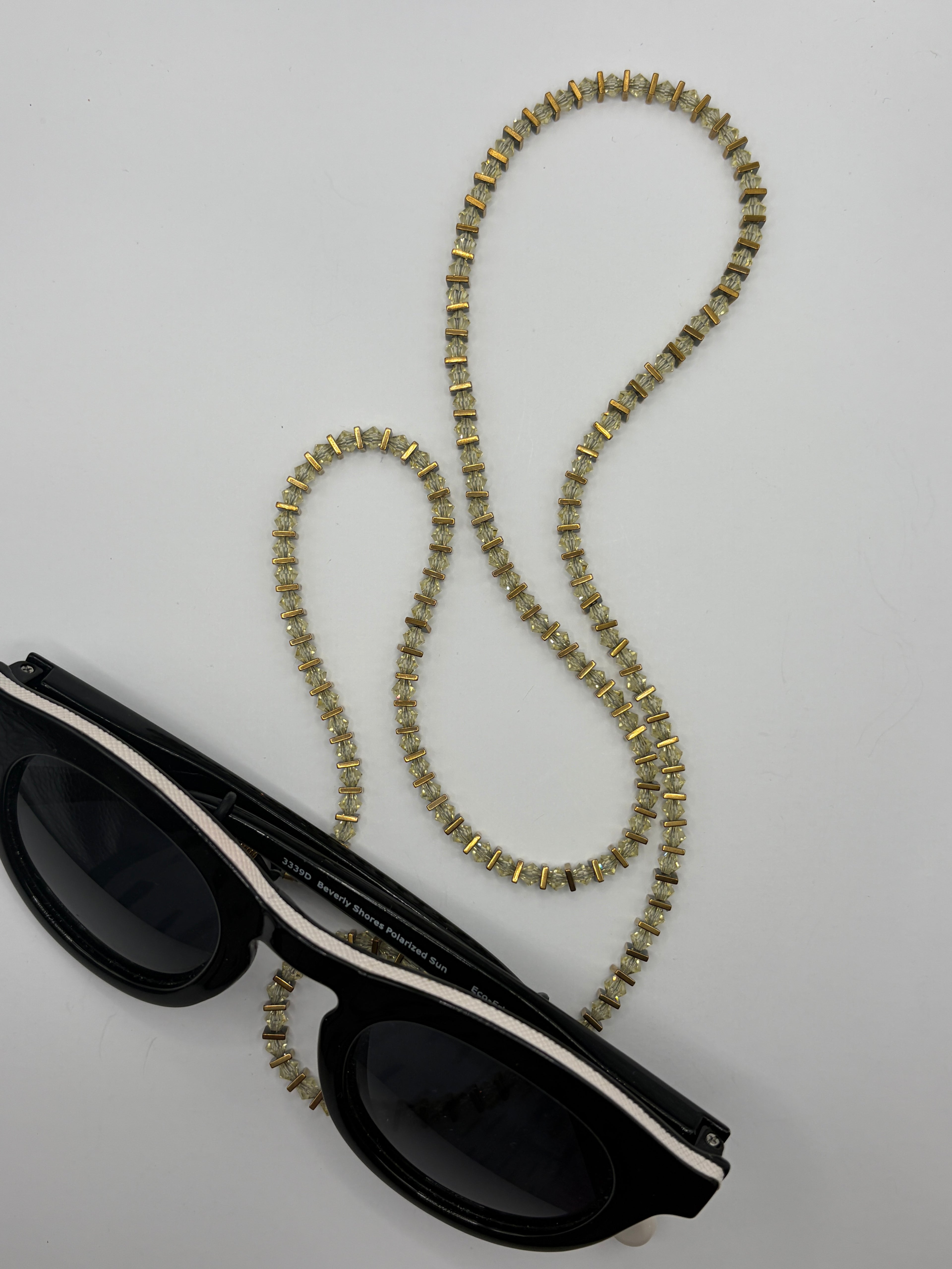 Black sunglasses with a decorative chain on a light gray background
