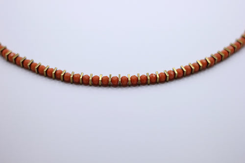 Necklace with orange beads and gold accents on a light gray background