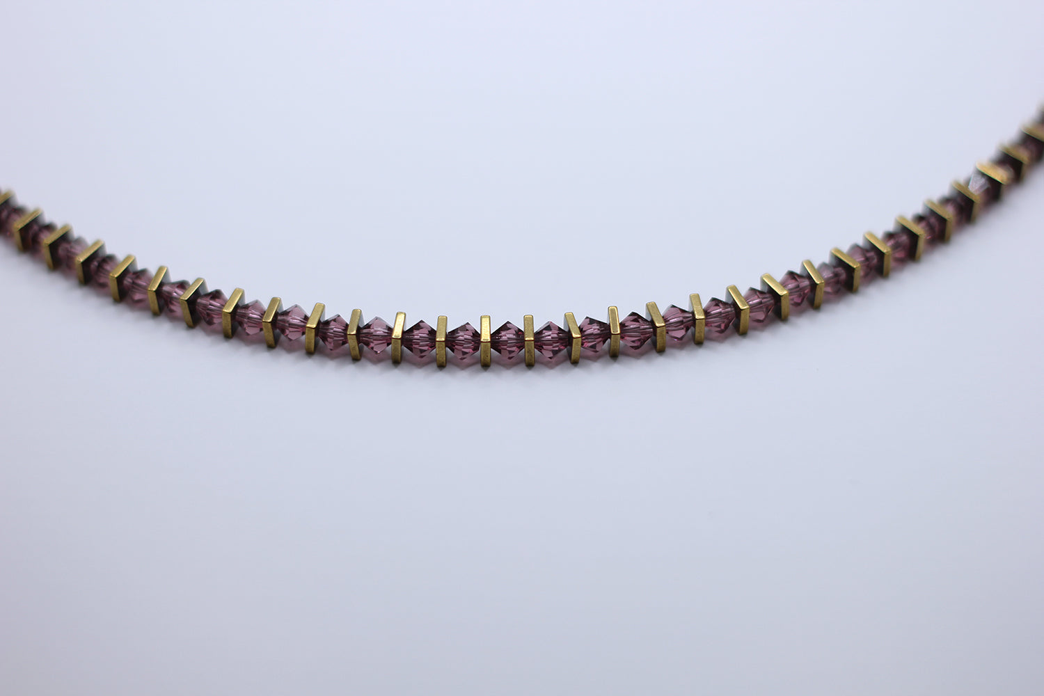 Necklace with purple merlot beads and gold accents on a light gray background