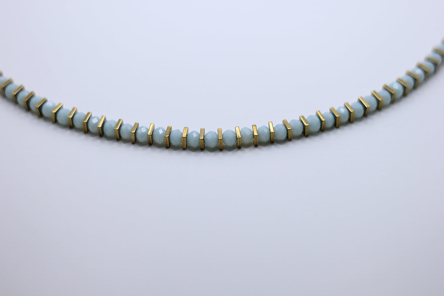 Necklace with light blue beads and gold accents on a light gray background