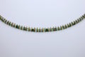 Necklace with green and gold beads on a light gray background